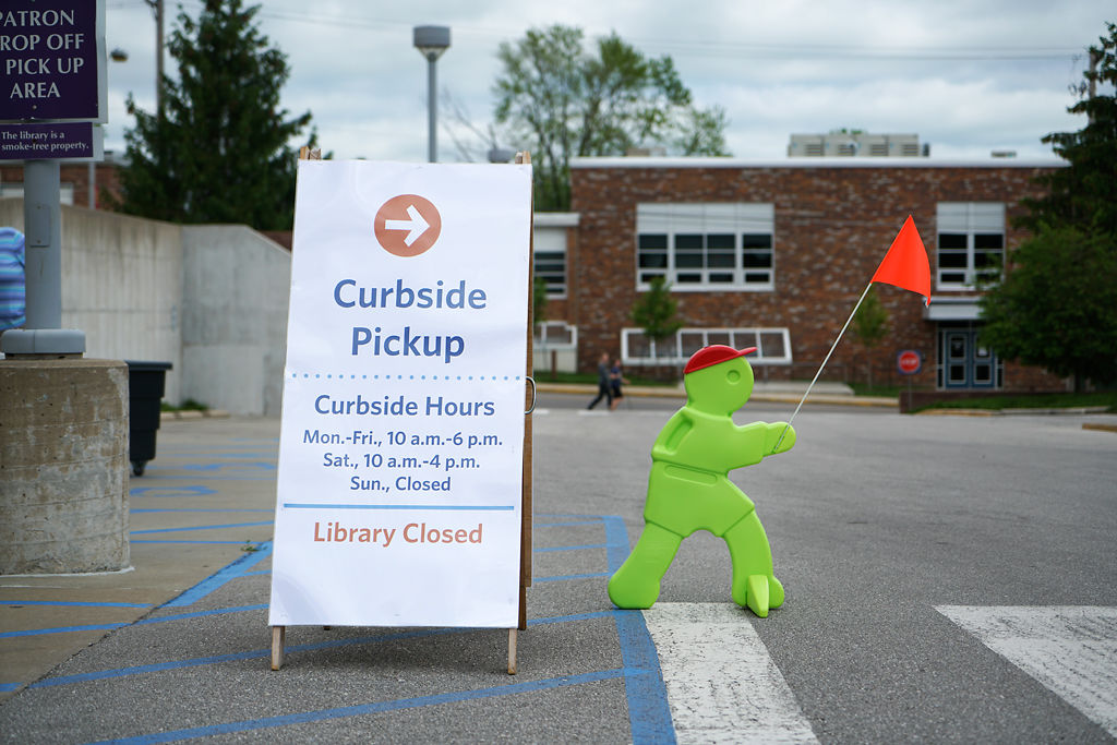 A roadside sign and a toy figure direct people to stop at designated spots and wait for books